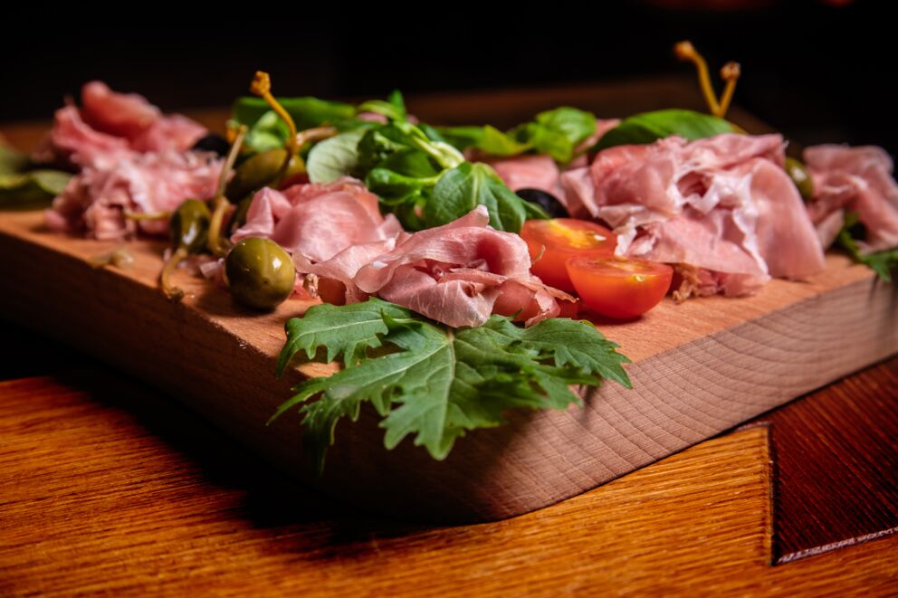 Rucola, Prosciutto, Tomaten, Kapern und Basilikum auf einem Holzbrett serviert im Restaurant Benediktus