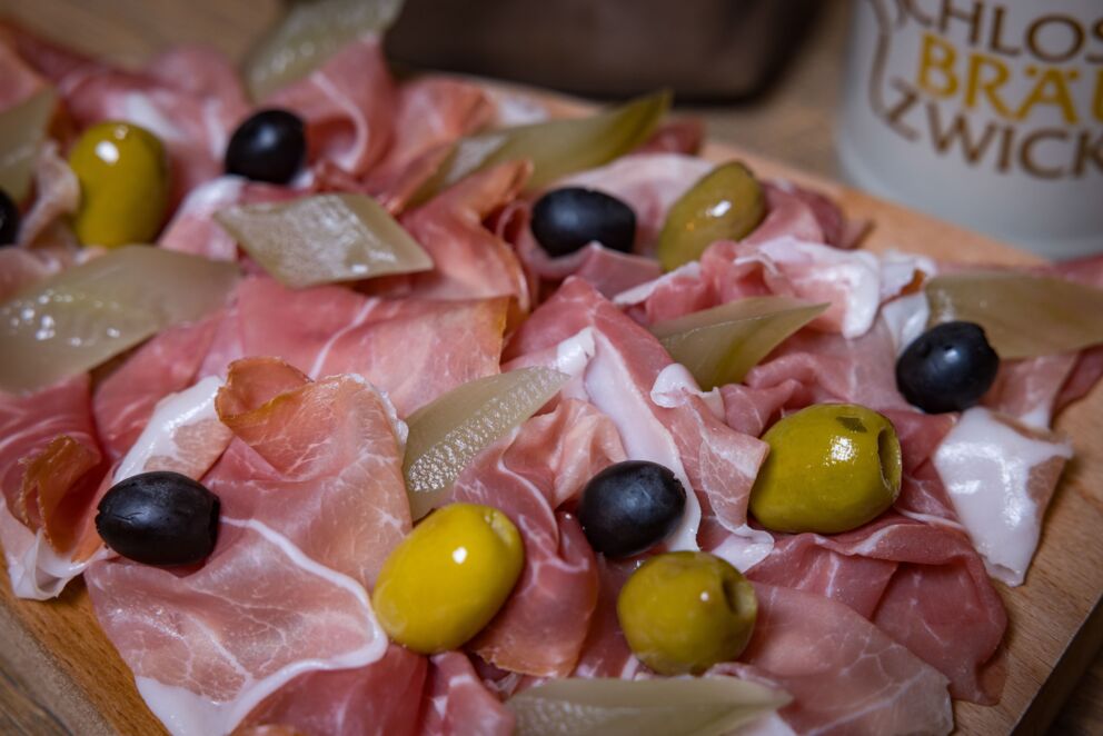 Speck mit schwarzen-grünen Oliven sowie mit Essiggurkenscheiben belegt
